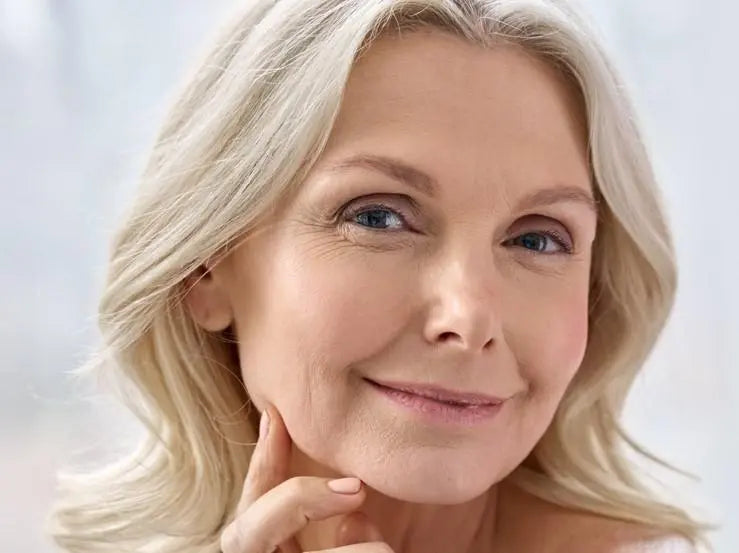 A mature woman with healthy hair and some wrinkles and fine lines around her eyes smiling at the camera