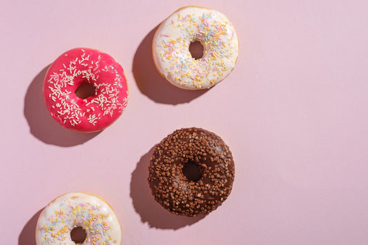 4 coloured doughnuts on a plain pink background as a sweet treat for mothers day