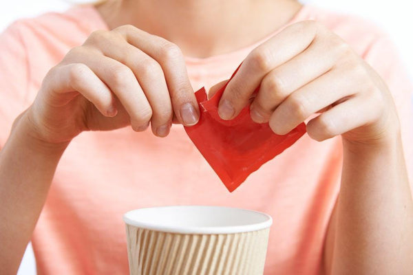 Picture of a woman adding a sweetener packet full of sugars and harmful additives to a cup of coffee.