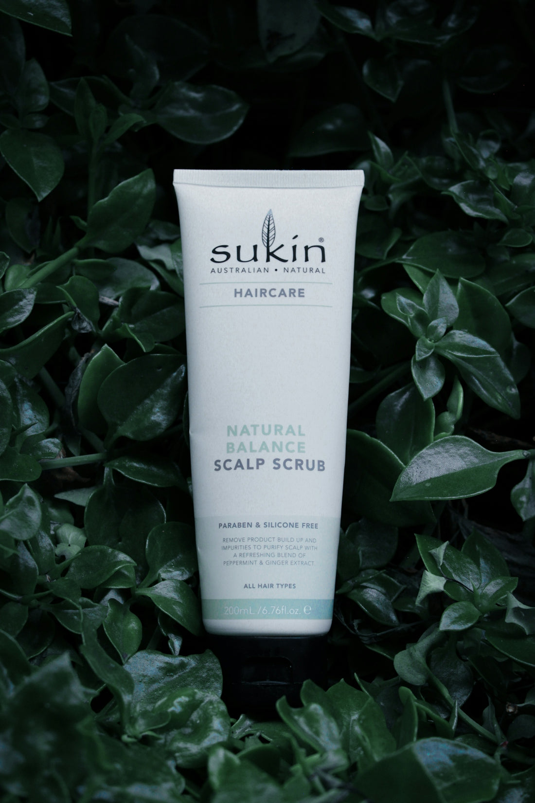a tube of sukin natural scalp scrub sitting in a bush