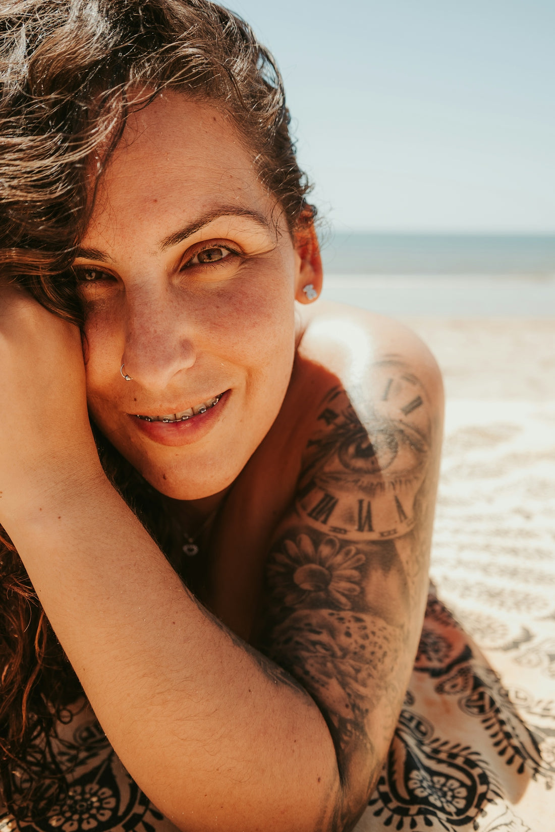 a woman laying on the beach with a tattoo on her arm