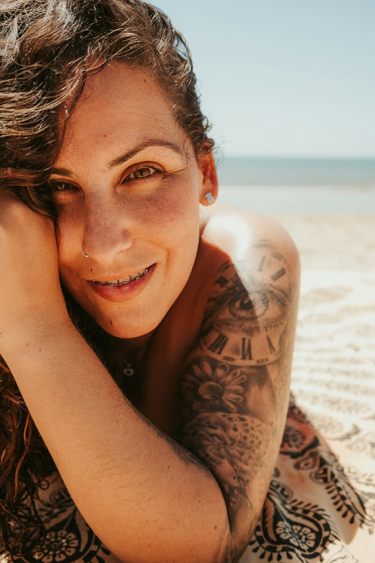 a woman laying on the beach with a tattoo on her arm