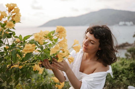a woman in a white dress is smelling a bush of yellow flowers