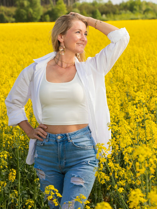 Woman poses in a field of bright yellow flowers.