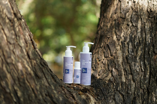 Three bottles of skincare products on a tree trunk.