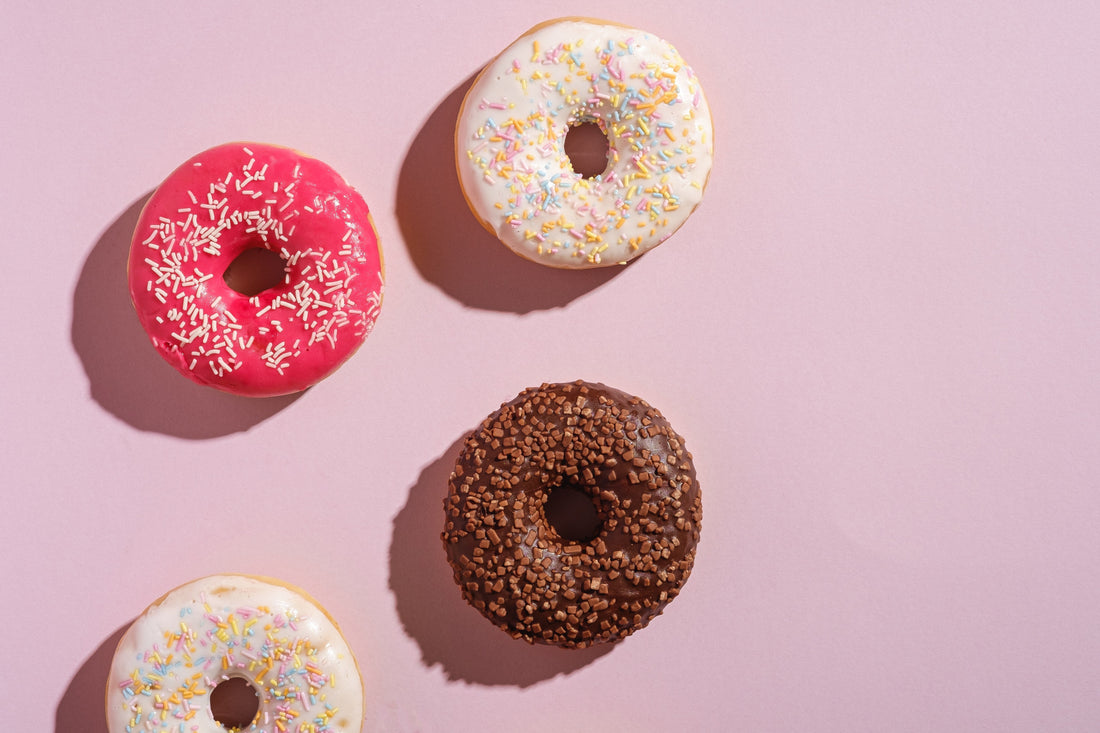 4 coloured doughnuts on a plain pink background as a sweet treat for mothers day